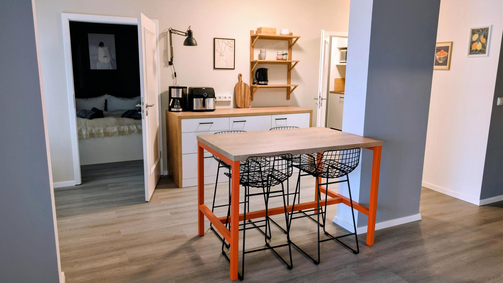 Essbereich mit Tisch und Stühlen, Küche und Schlafzimmer im Hintergrund.
