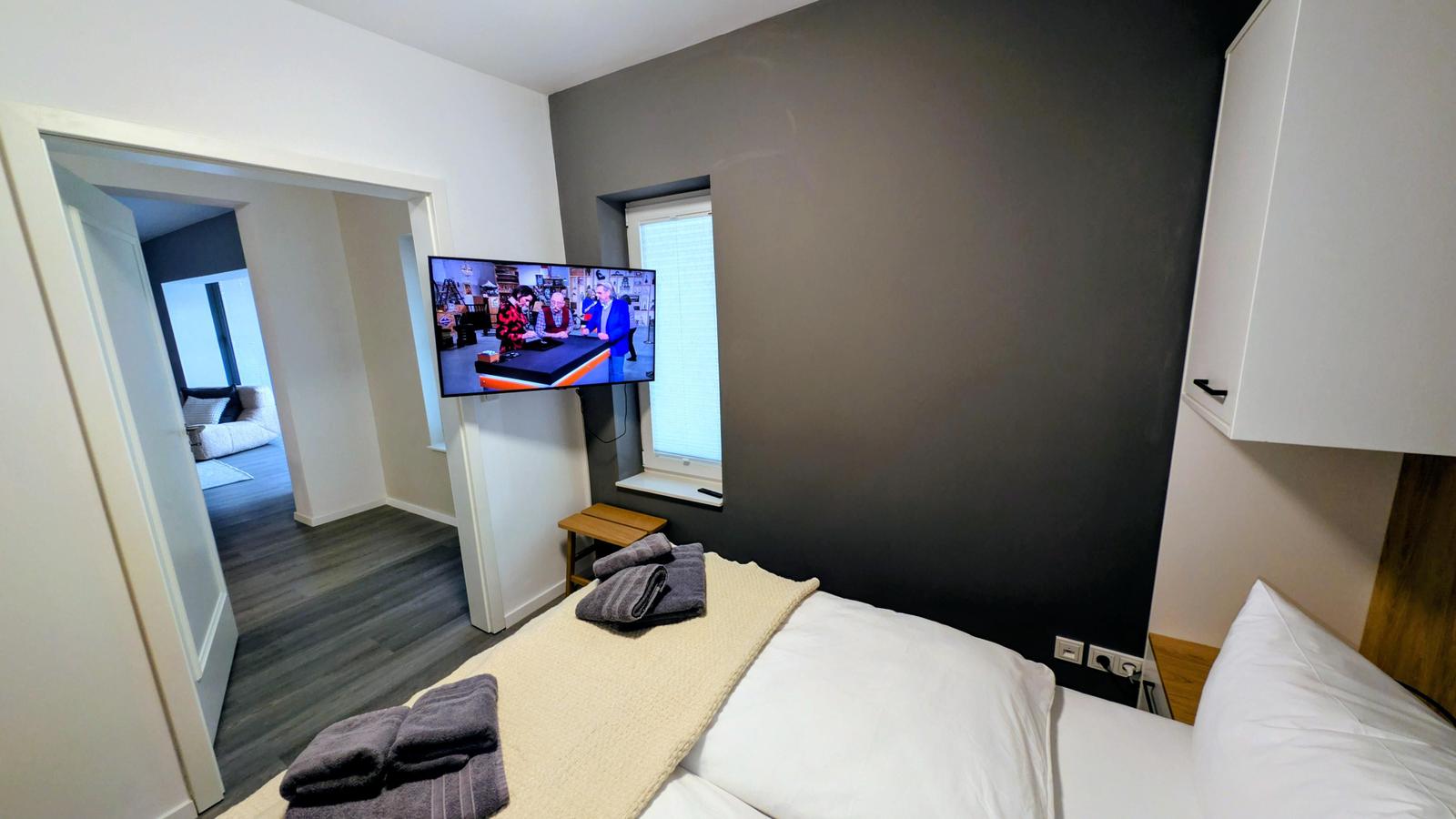 Schlafzimmer mit Bett, Fernseher und Blick in Wohnbereich.