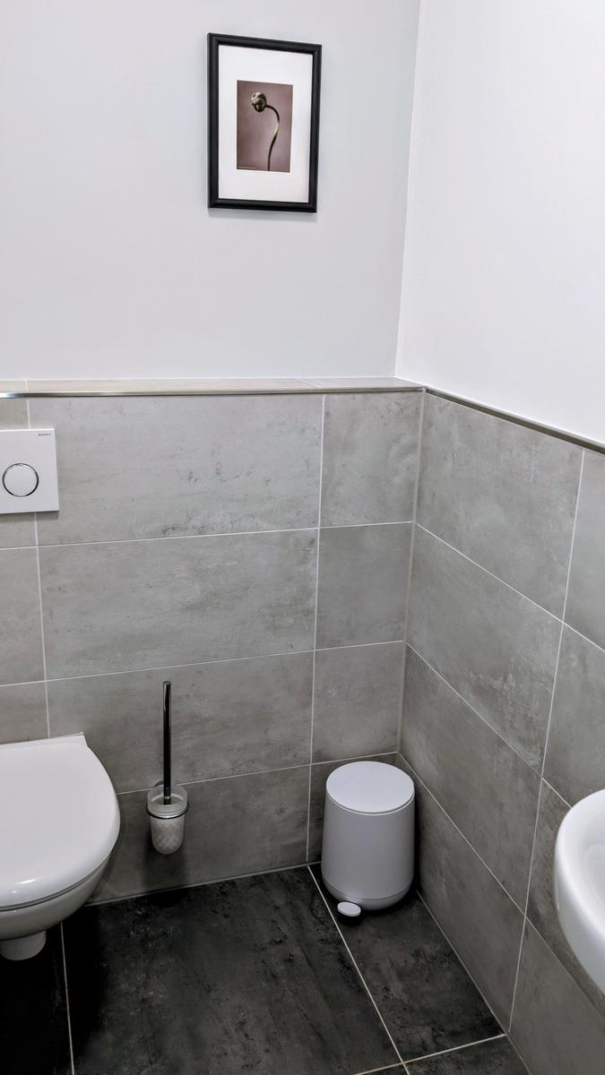 Badezimmer mit Toilette, Spüle und Mülleimer an der Wand.
