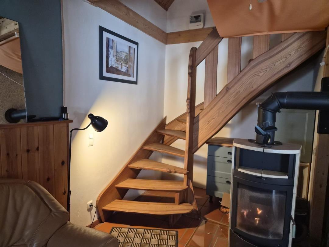 Wooden staircase leads upstairs. Fireplace and wall picture are visible.