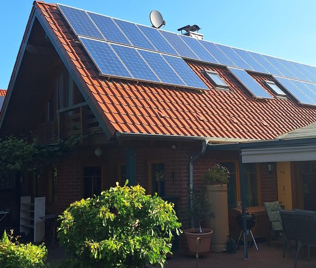House with solar panels on roof, terrace with garden furniture and plants.