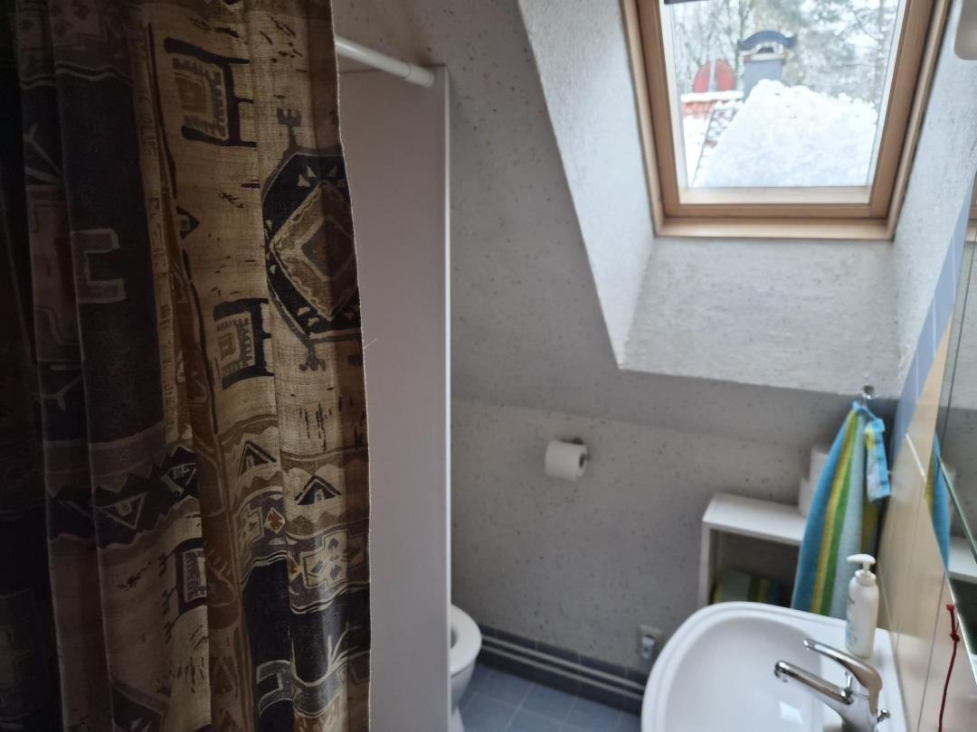 Bathroom with shower, toilet, and sink under sloped roof with window.