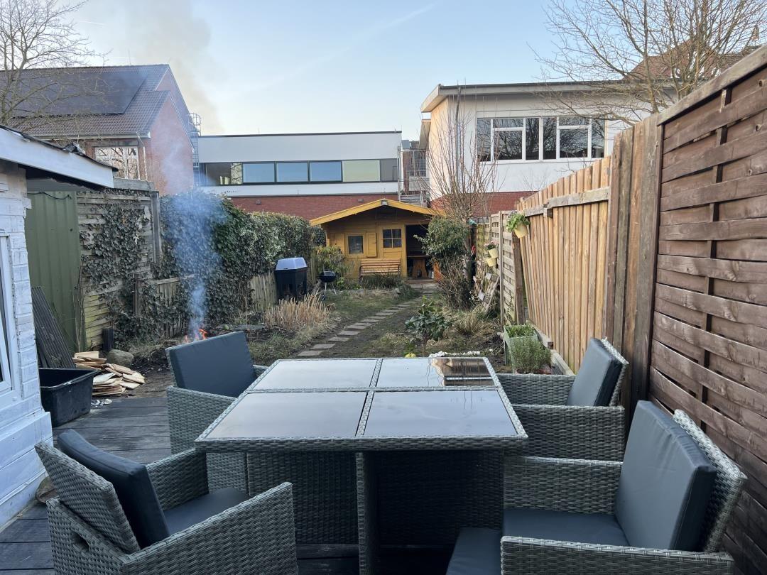 Terrace with seating group, grill, and small wooden house in background.