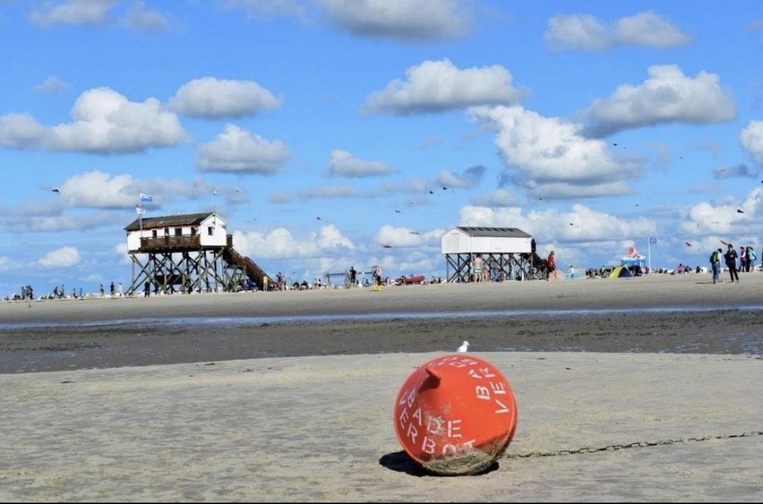 Beach with tidal flats, red buoy, and wooden beach huts in the background.