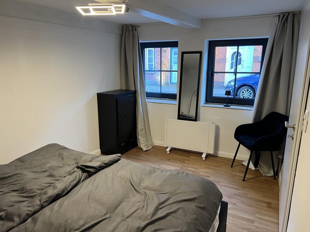 Bedroom with bed, wardrobe, mirror and windows. Wooden floor and black furniture.