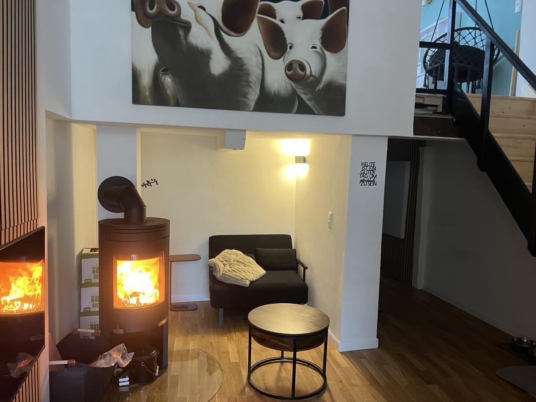 Living area with wood stove, sofa, and wall painting of pigs.