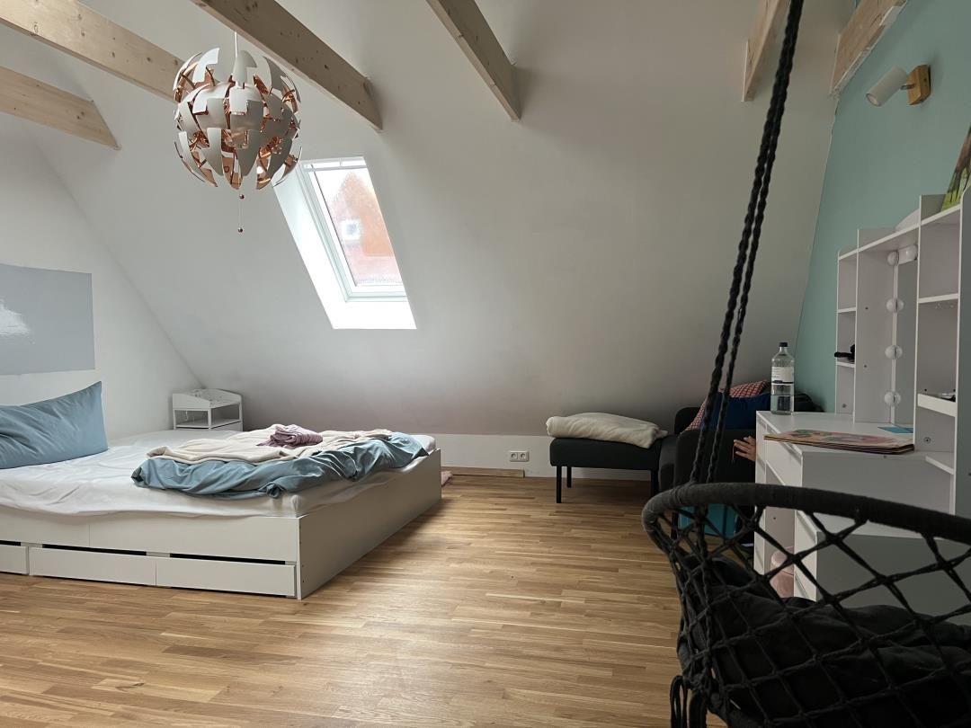 Bedroom with sloped ceiling, bed, desk, and hanging chair.