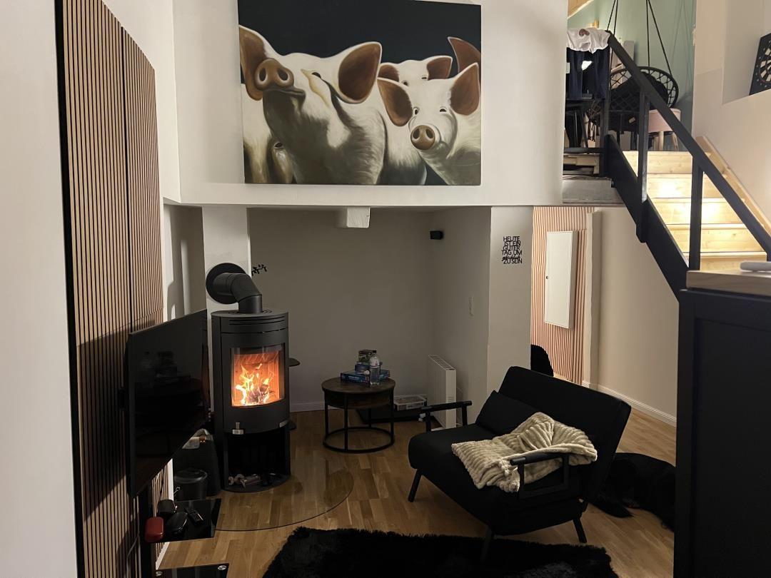Living area with fireplace, armchair, and wall painting of pigs.