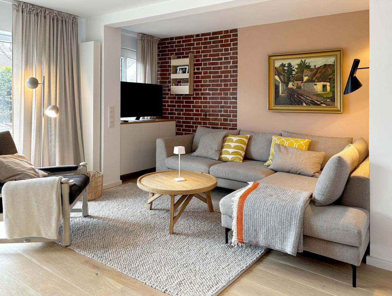 Wohnzimmer mit Sofa, Couchtisch und Fernseher an Backsteinwand.