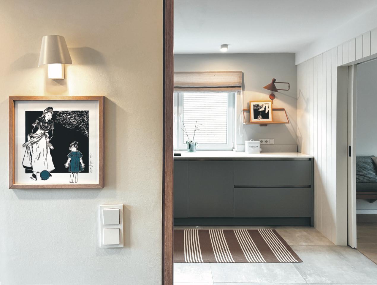 Küche mit dunklen Schränken, Fenster und Teppichboden. Wandbild und Wandlampe sichtbar.