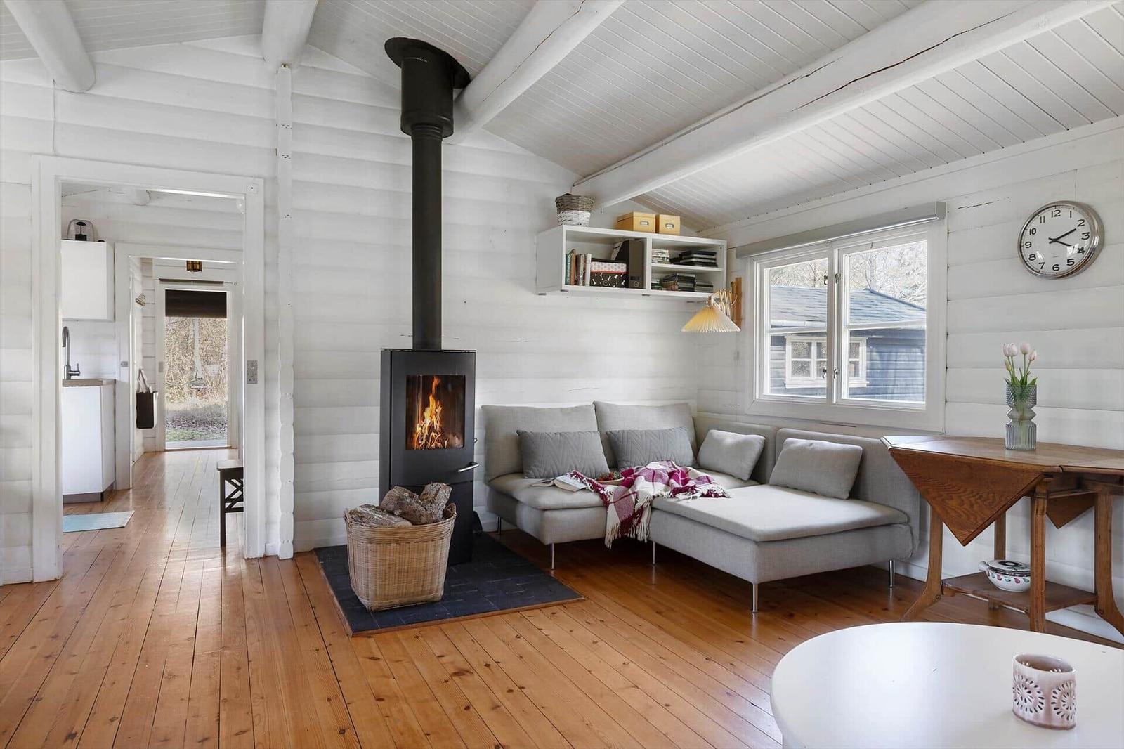 Living room with fireplace, sofa, and wooden floor. Kitchen in background.