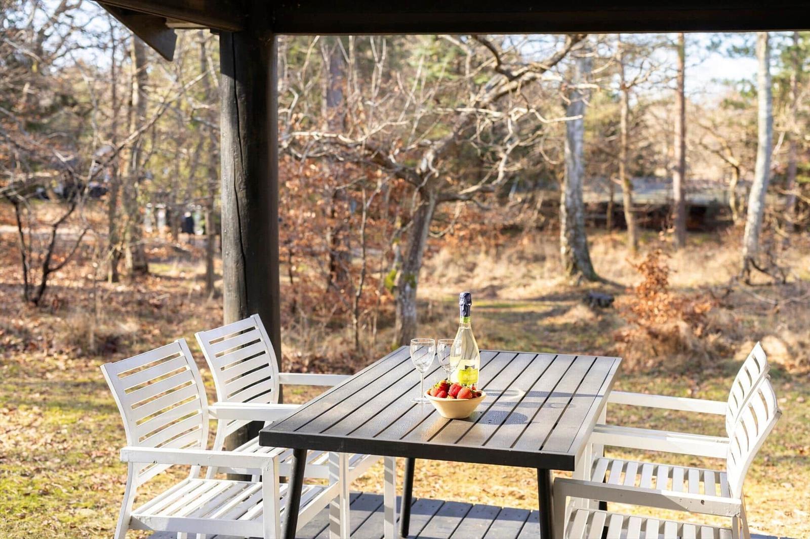 Patio with table and chairs, featuring a bottle and bowl of strawberries.