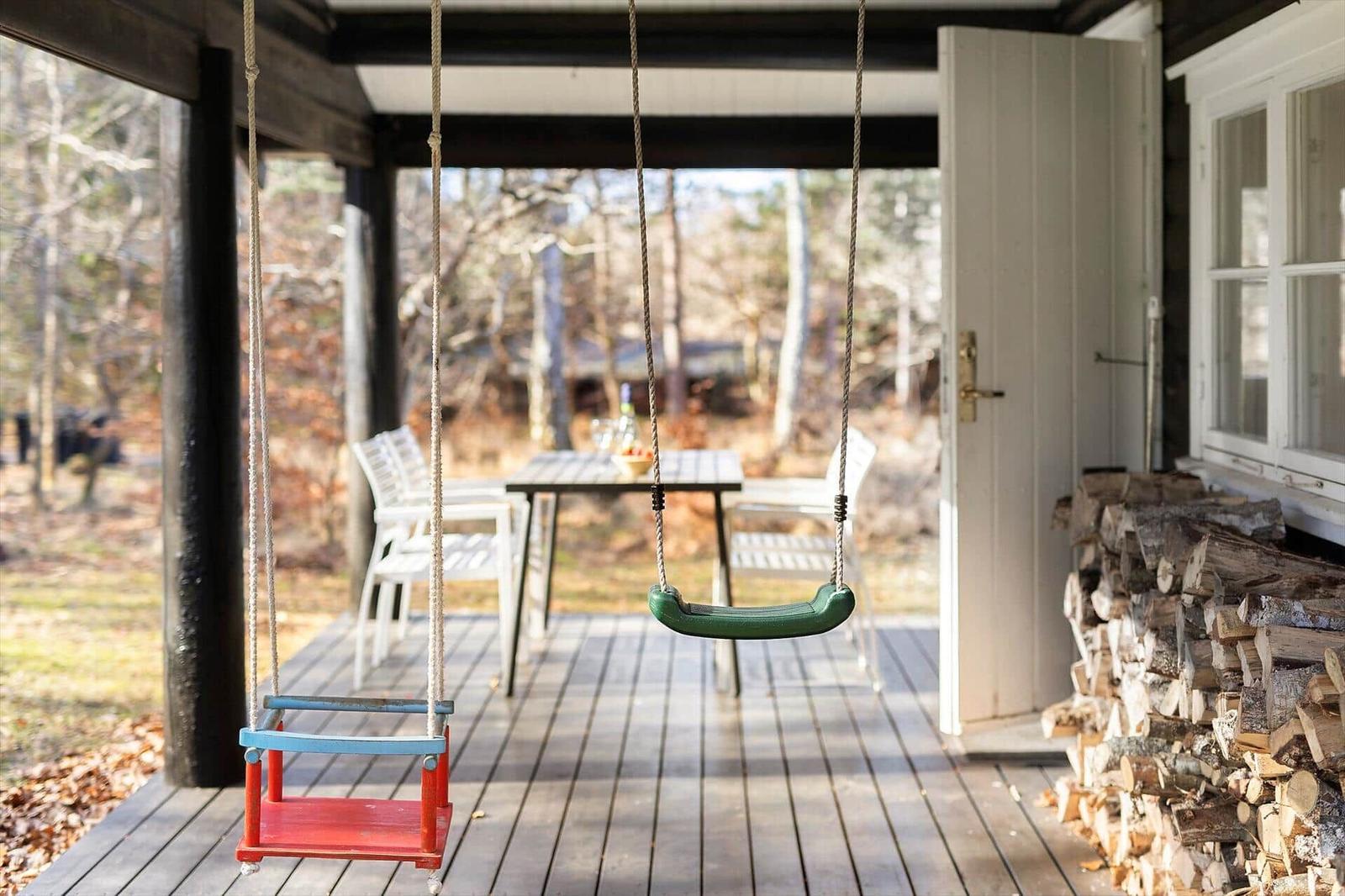 Patio with swings, table and chairs, woodpile and forest view.
