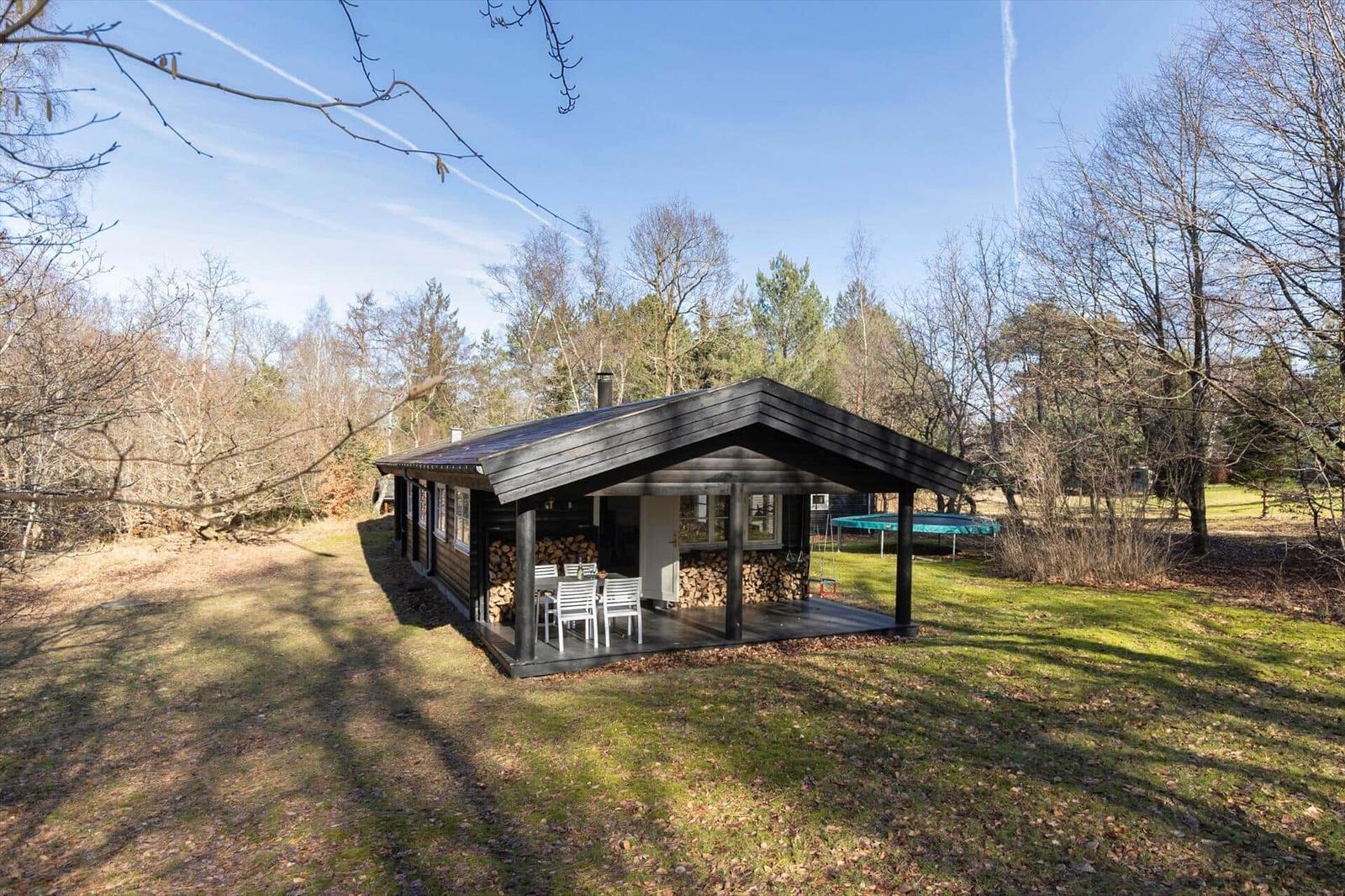 Wooden cabin with terrace, grill area, and trampoline in the woods.