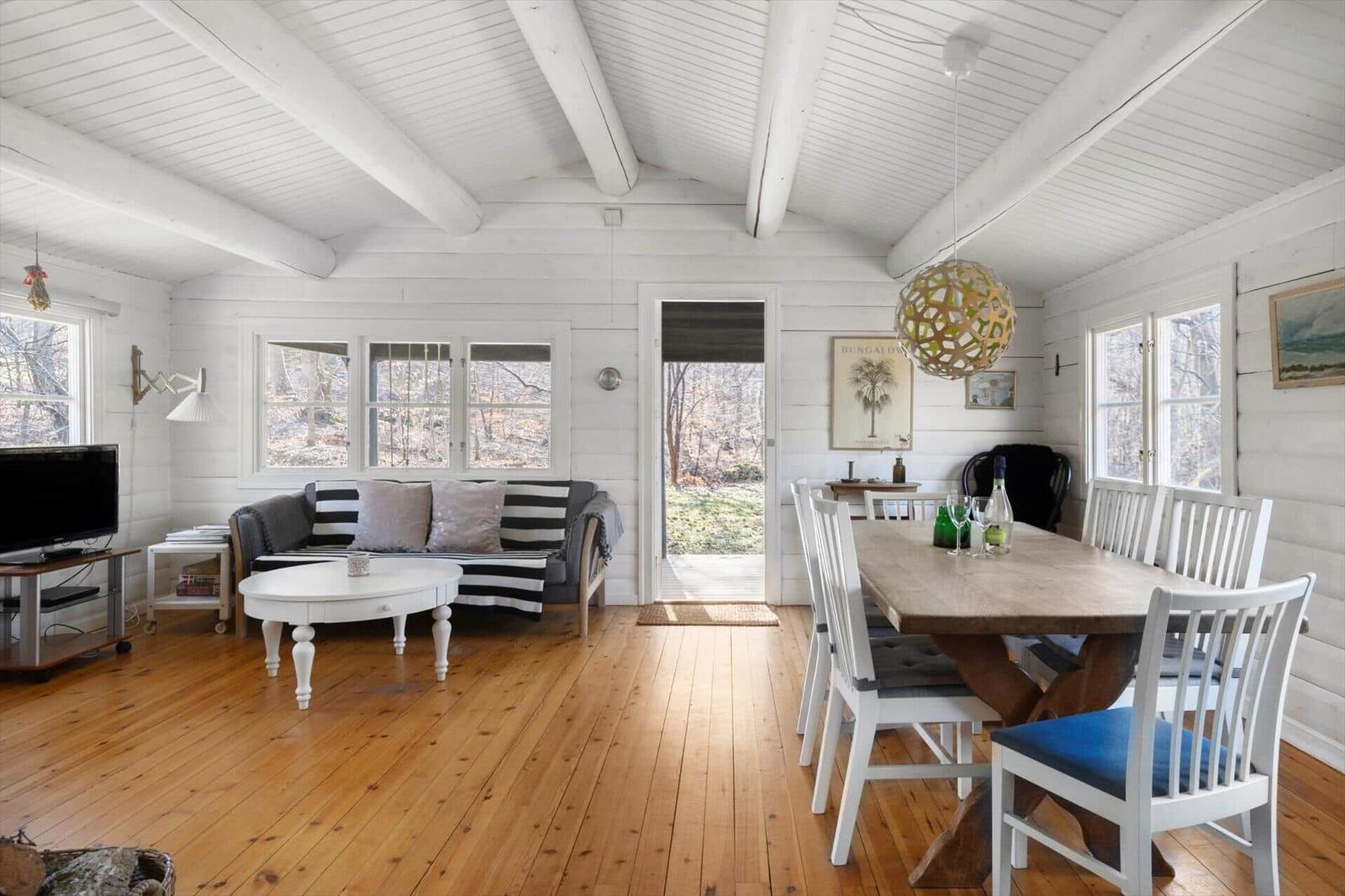 Living and dining area with wooden floor, white wall paneling, and table with chairs.