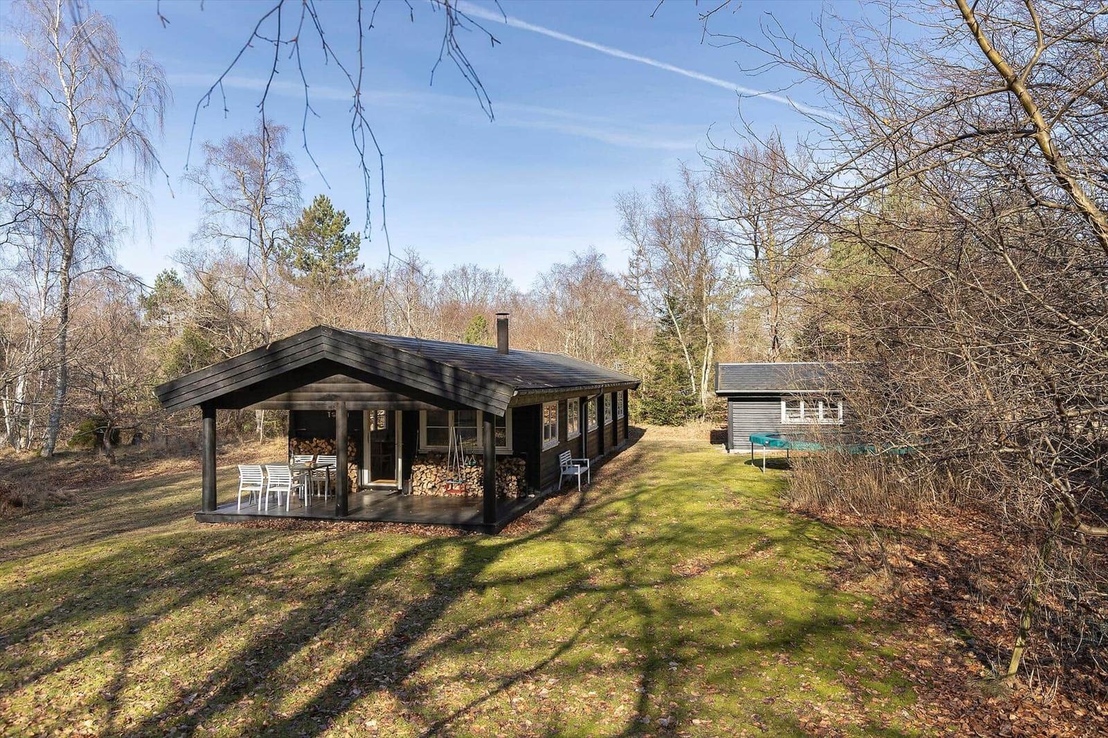 Wooden house with terrace, garden, and small outbuilding in woodland.