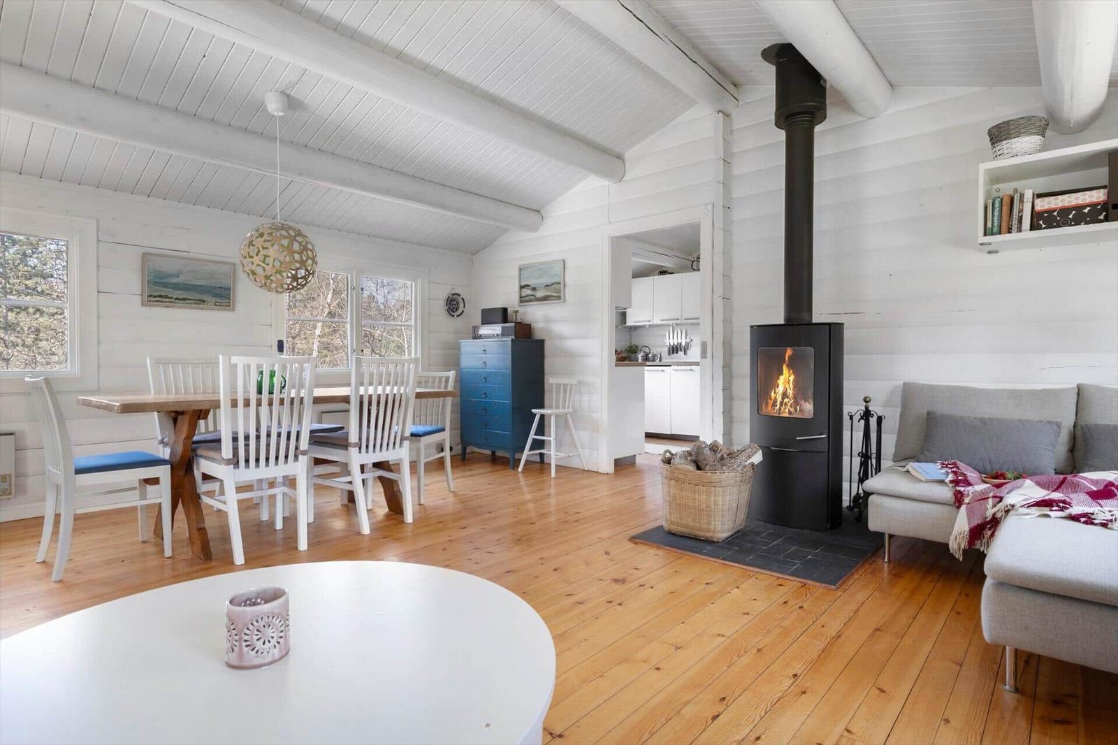 Living and dining area with fireplace, wooden floor, and white wood paneling.