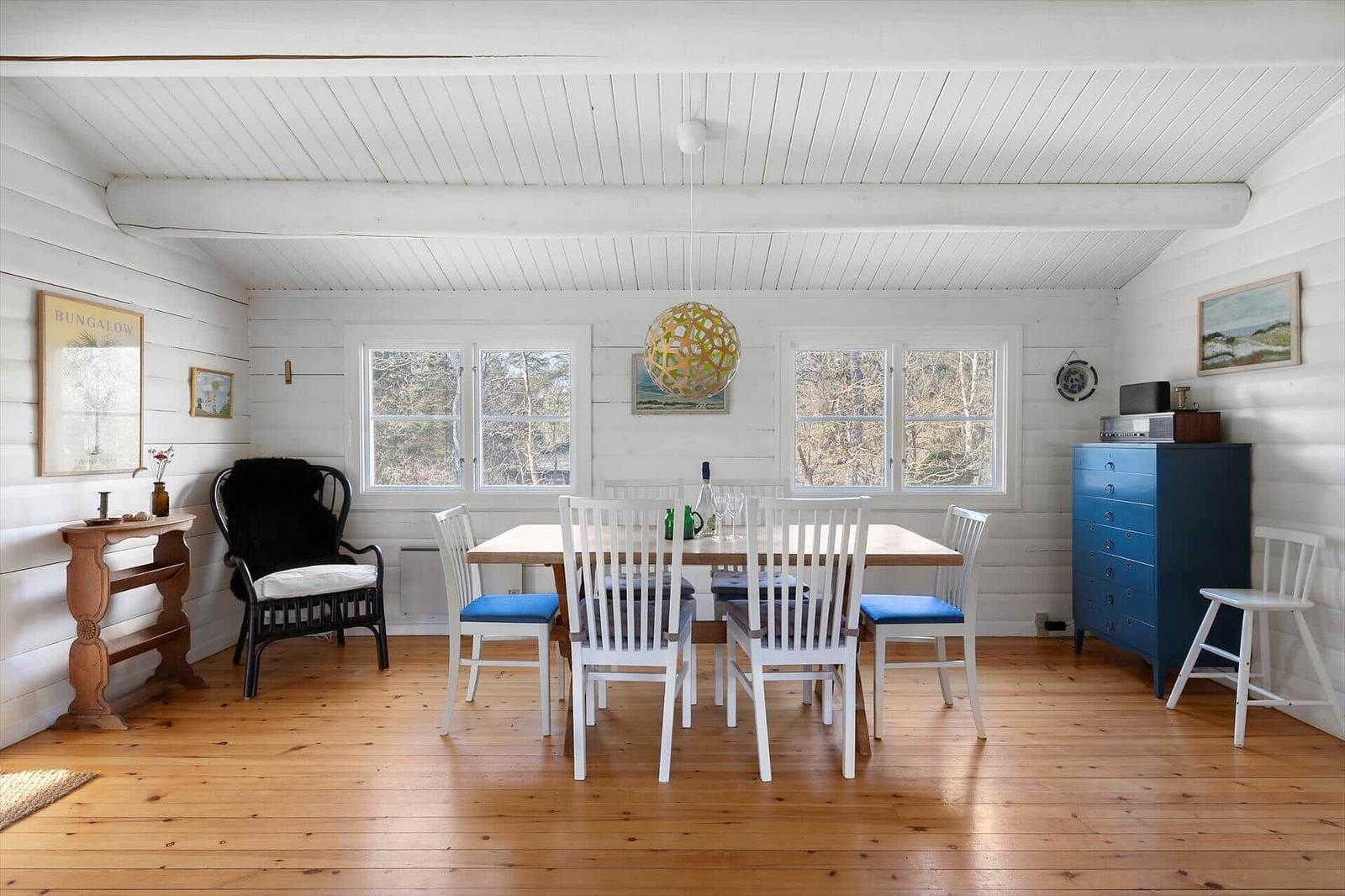 Dining room with wooden floor, white table, blue seat cushions, and blue cabinet.