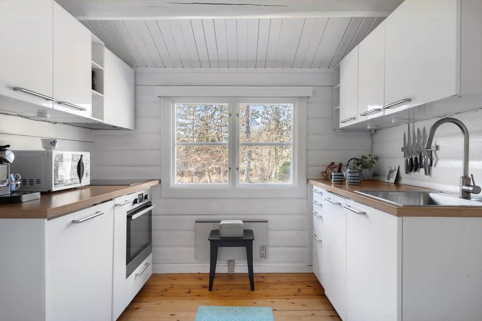 Kitchen with white cabinets, wooden countertops, and window view of trees.