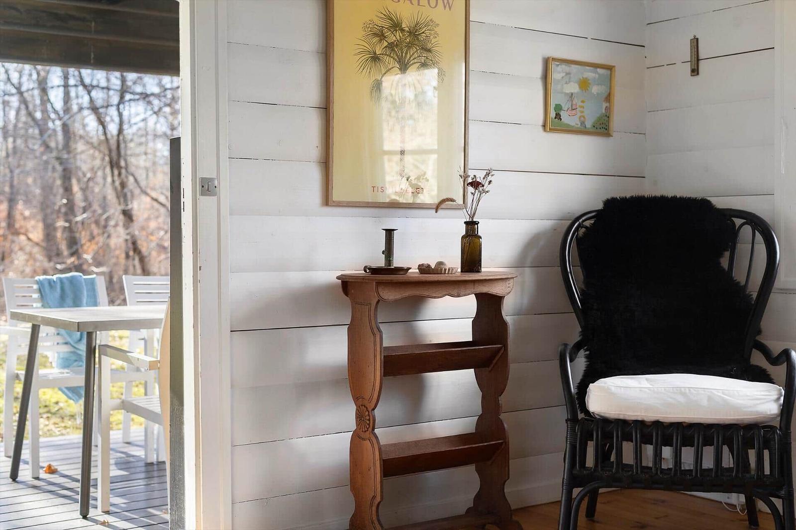 A room with white wood paneling, a black chair with fur, and a wooden table.