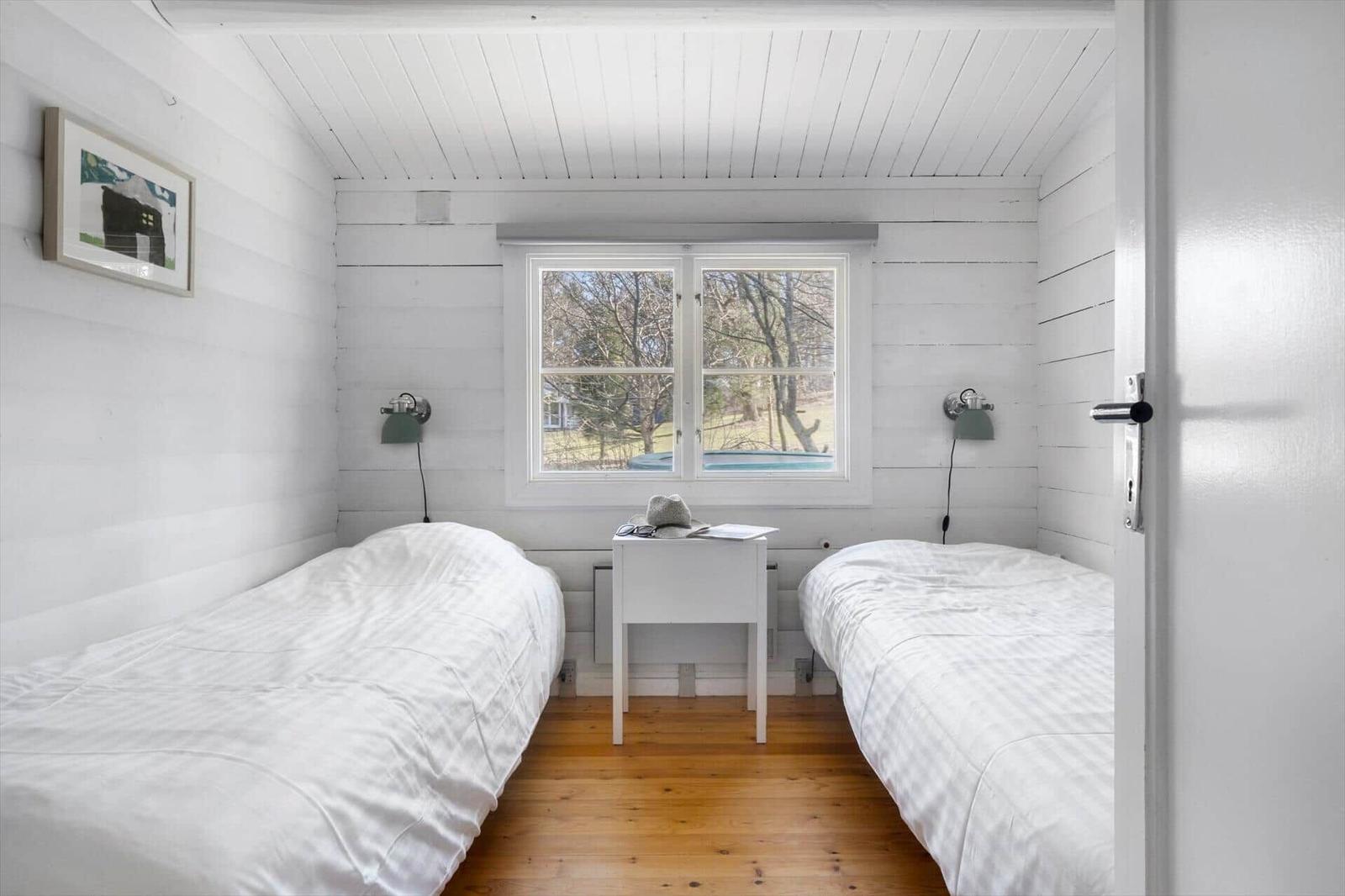 Two beds, one window, wooden floor, white walls.
