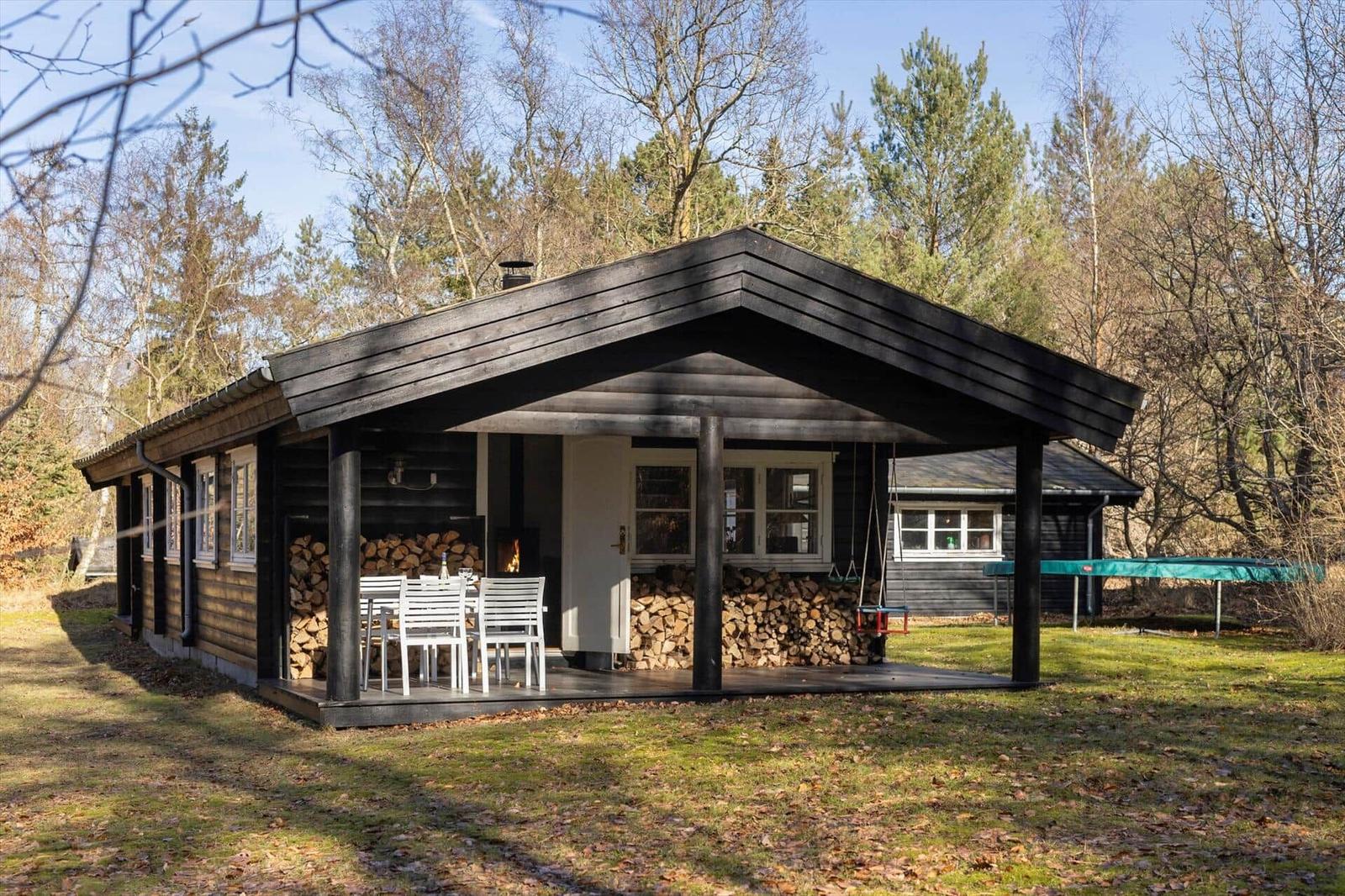 Wooden cabin with covered area, grill, and seating in the forest.