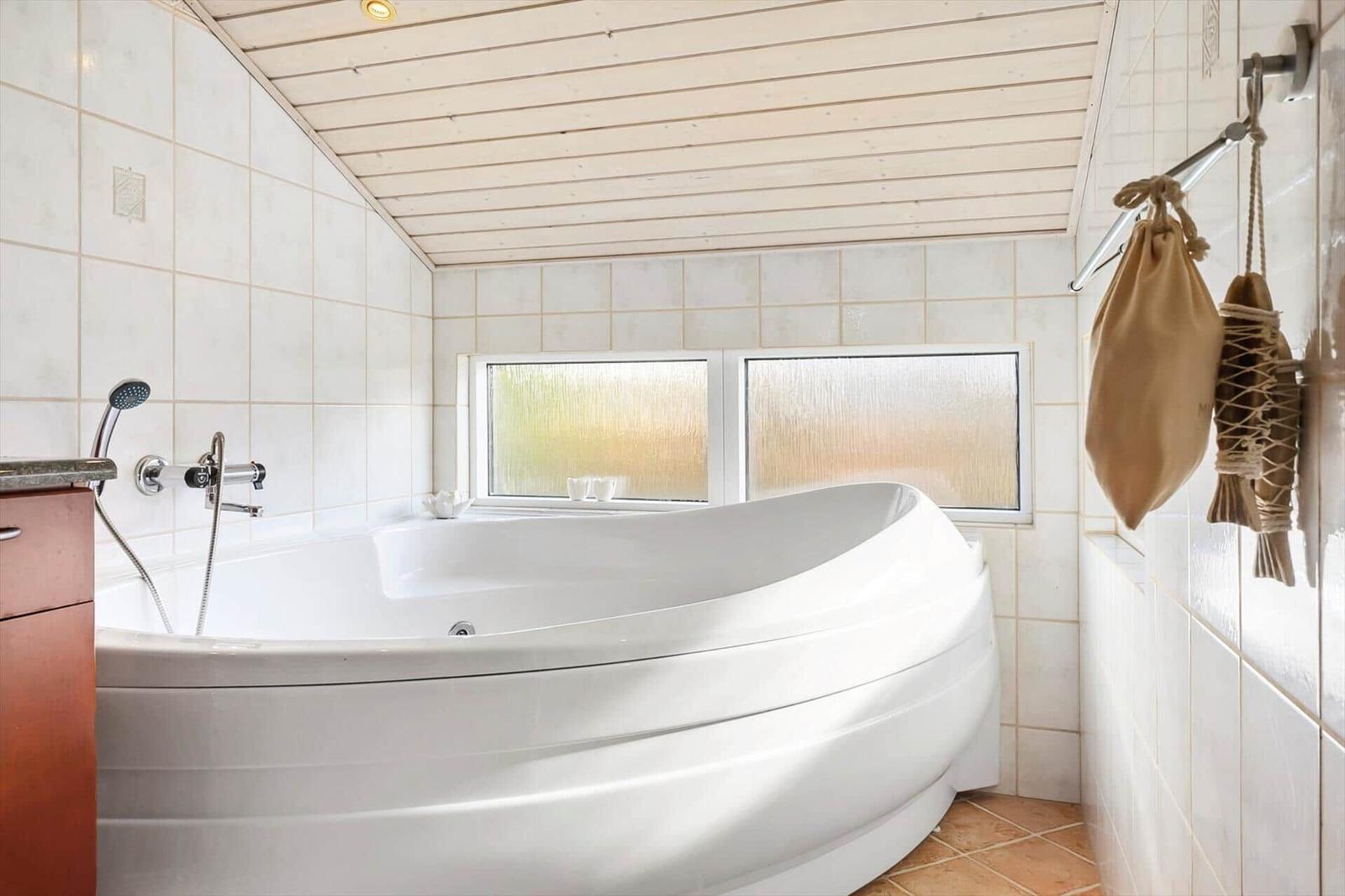 Bath with whirlpool, tiled walls, and two windows with frosted glass.
