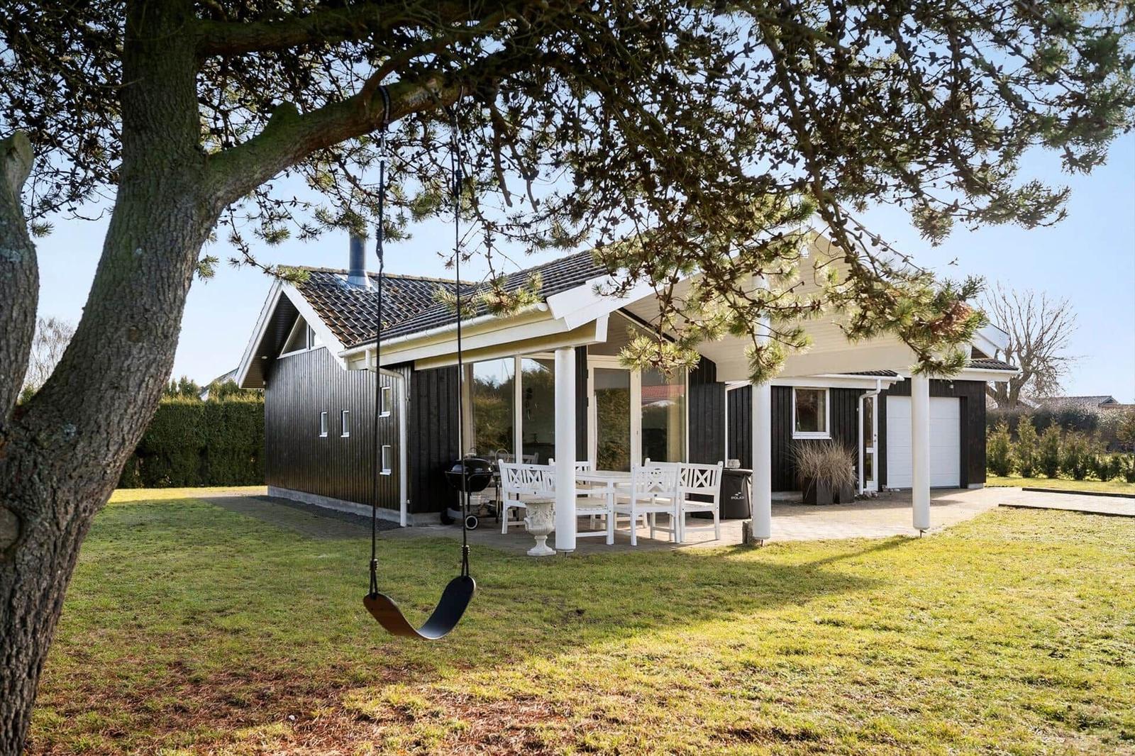 House with terrace, grill, and swing under tree.