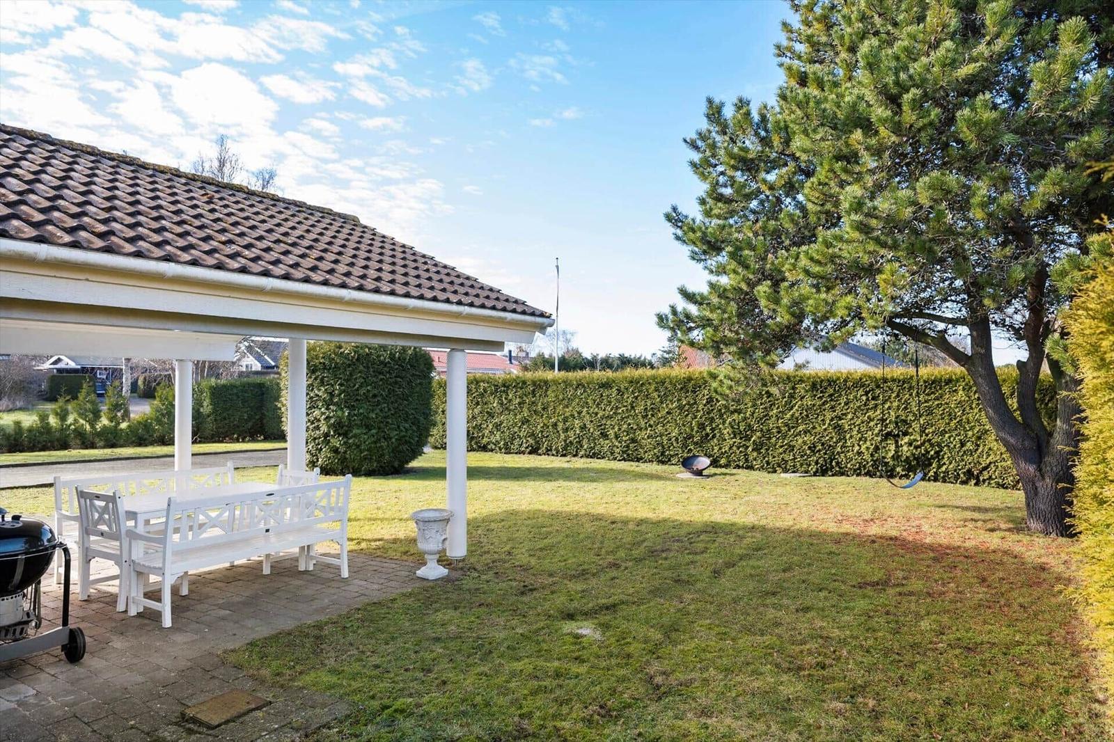Garden with pavilion, white table and chairs, grill and large tree.