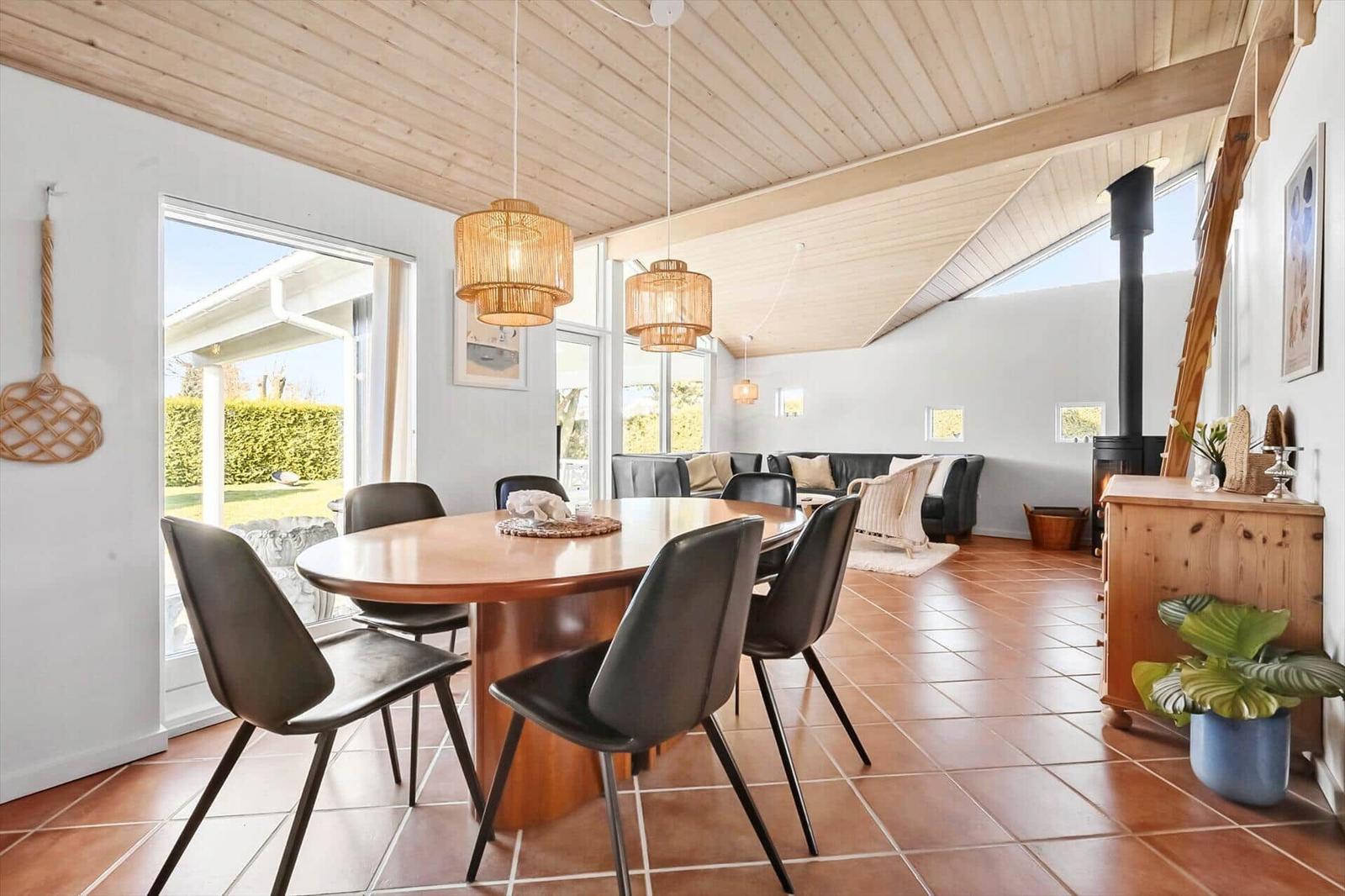 Dining area with round table and chairs. Living area with sofa and stove. Wooden ceiling and terrace door.