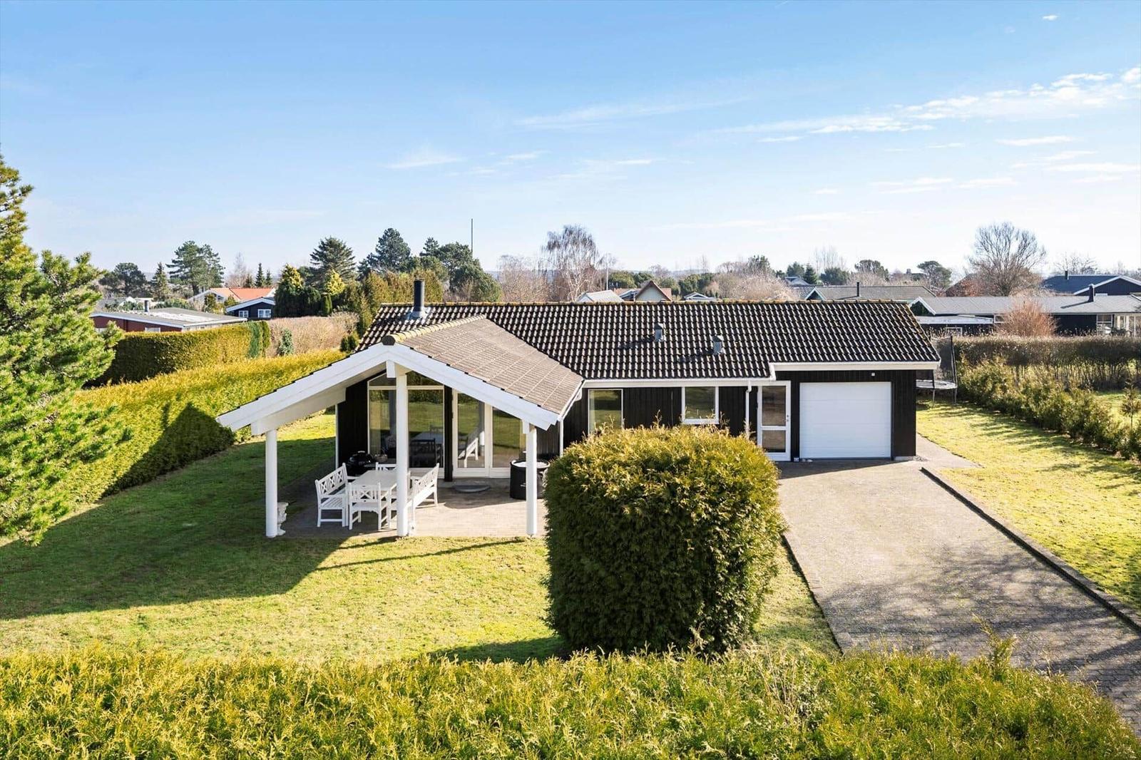 Single-story house with terrace, grill, and garage on green grounds.