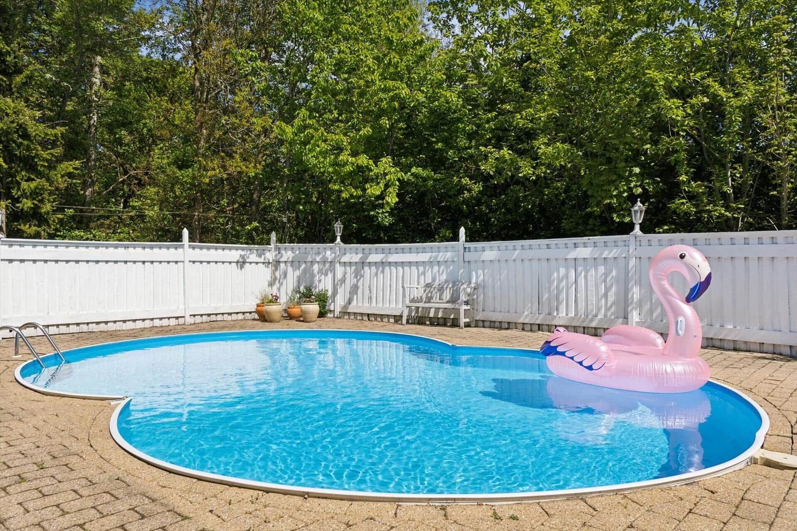 A round pool with a pink flamingo float and a white fence surrounding it.