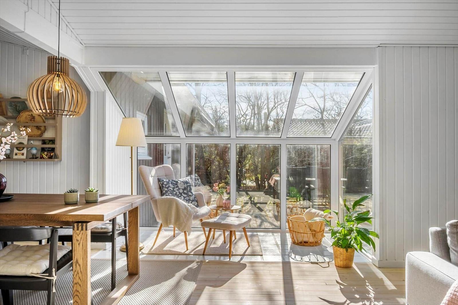 A room with large glass front, wooden table, armchairs and plants.