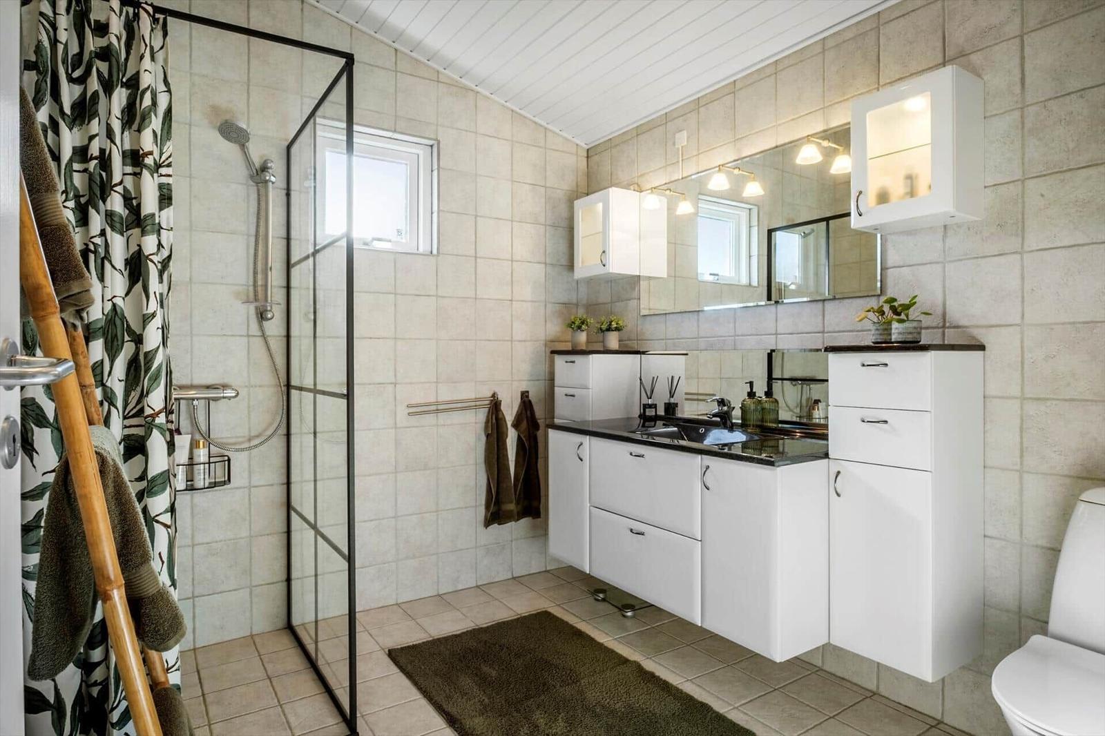 Bathroom with shower, sink and toilet. White cabinets, mirror and tiles.