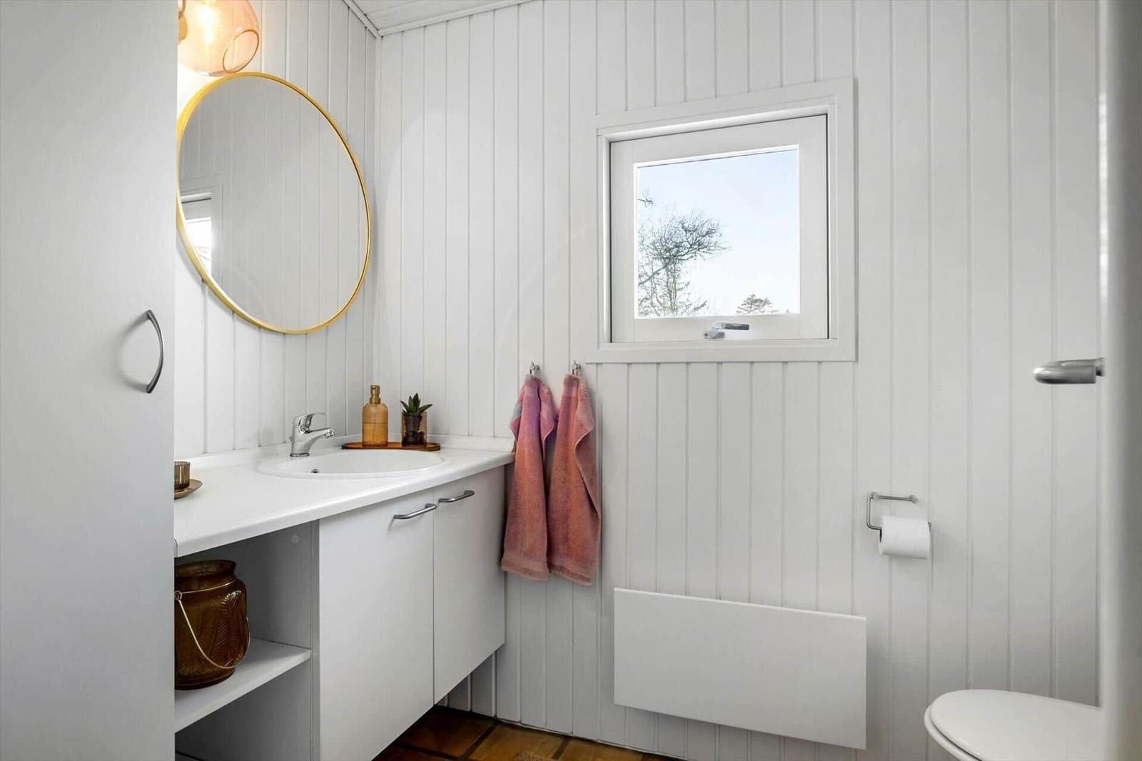 Bathroom with sink, mirror, and toilet. Window and towels visible.