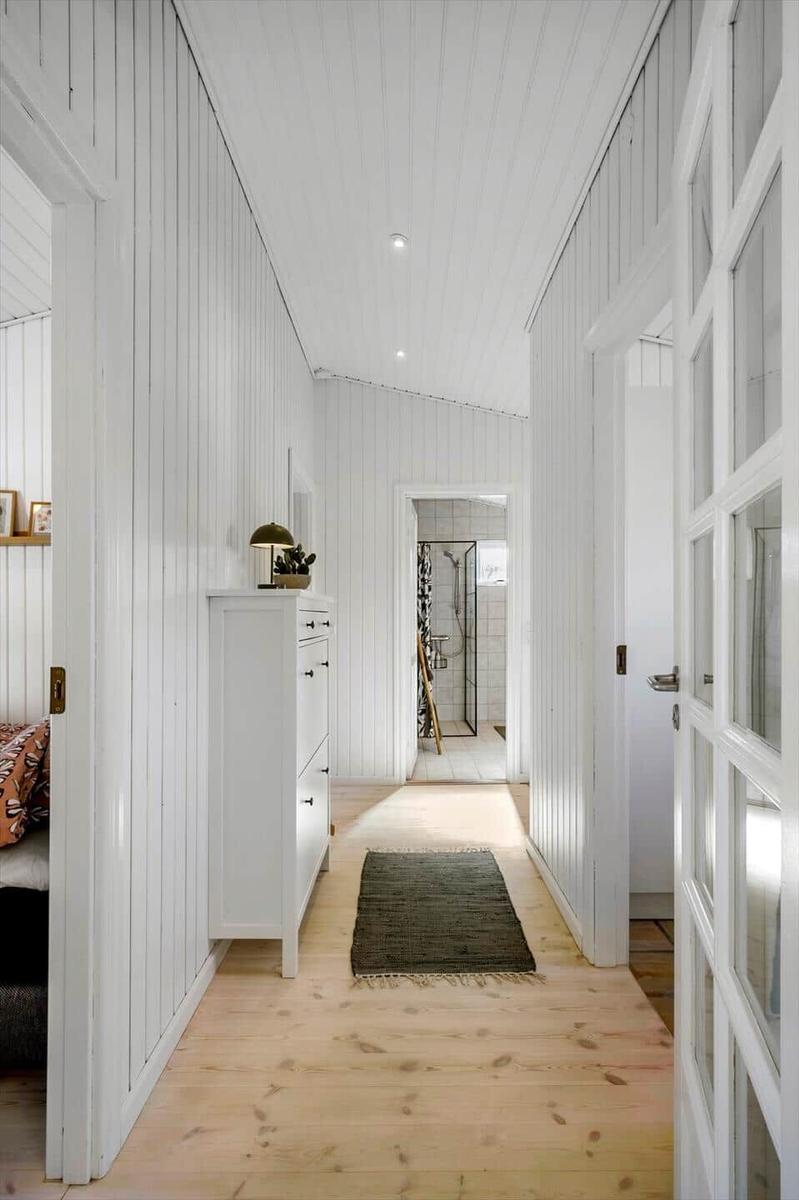 Hallway with white walls, wooden floor, and cabinet. Passage to the shower.