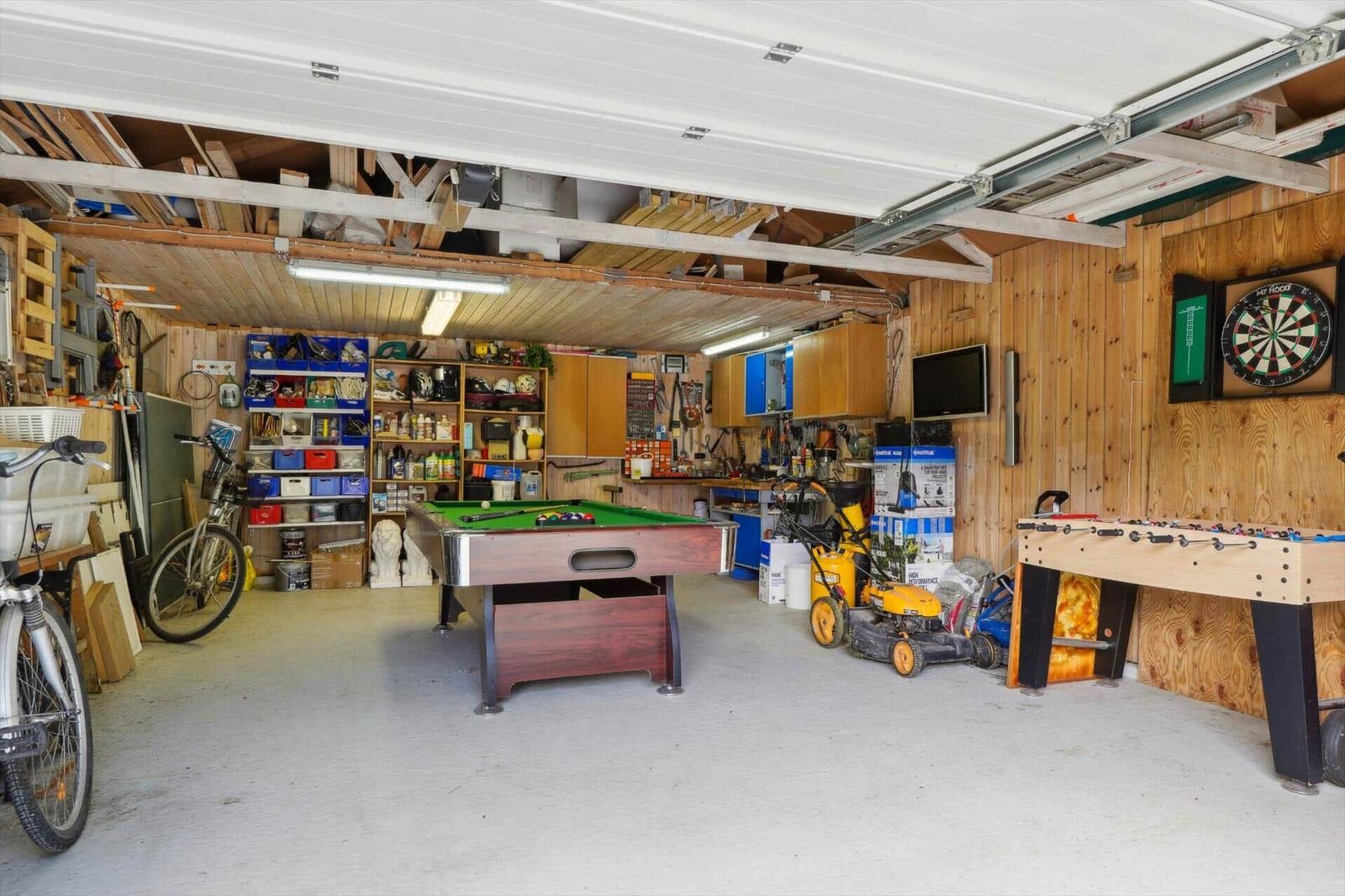 Garage with pool table, dartboard, foosball table, tool shelves, and lawnmower.
