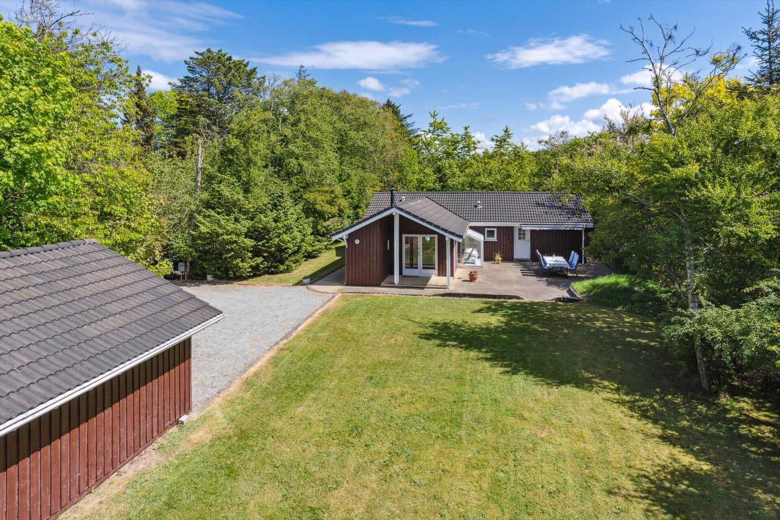 A house with terrace and garden surrounded by trees under blue sky.