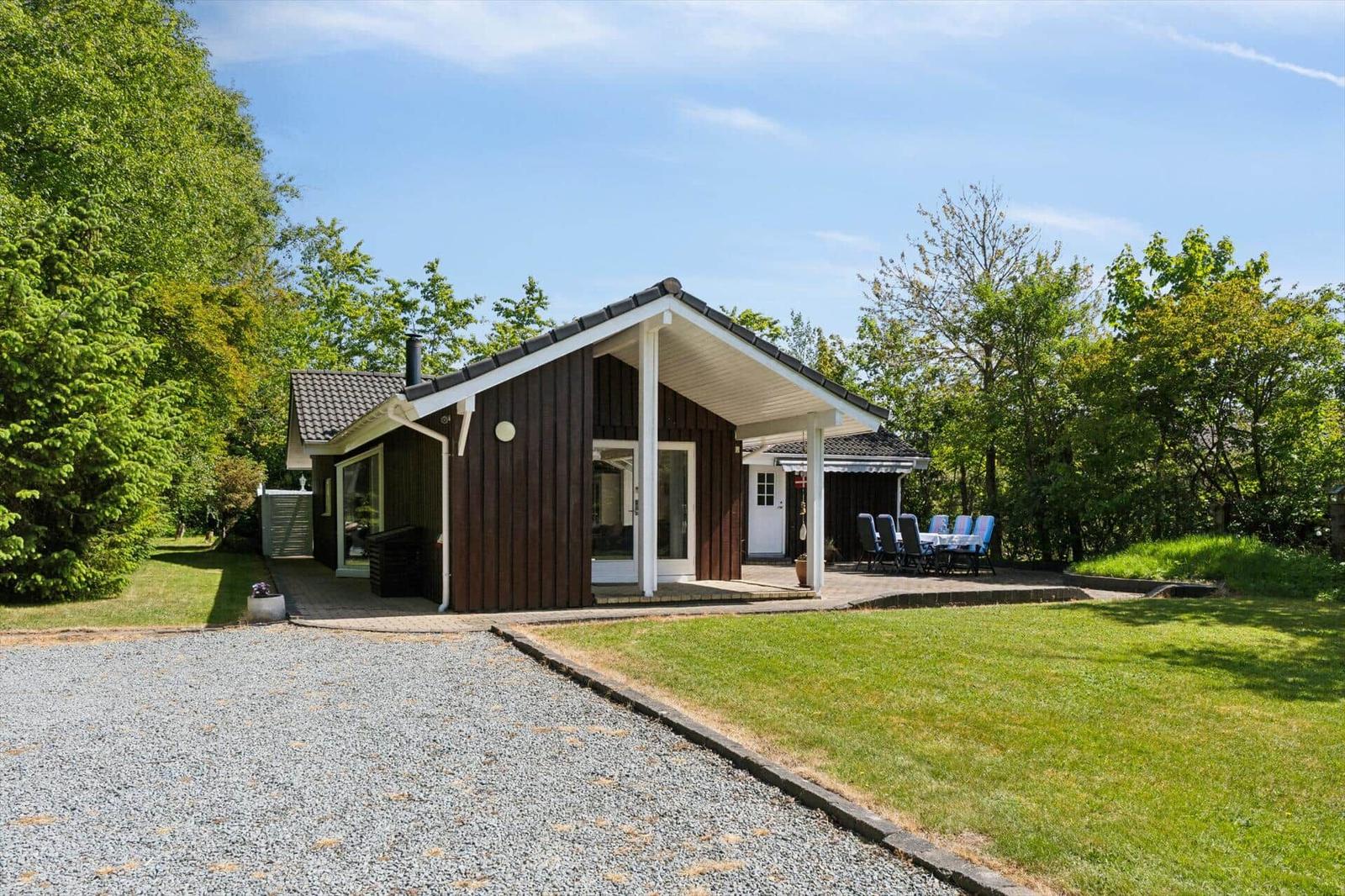 Wooden house with terrace, garden, and barbecue area in greenery.