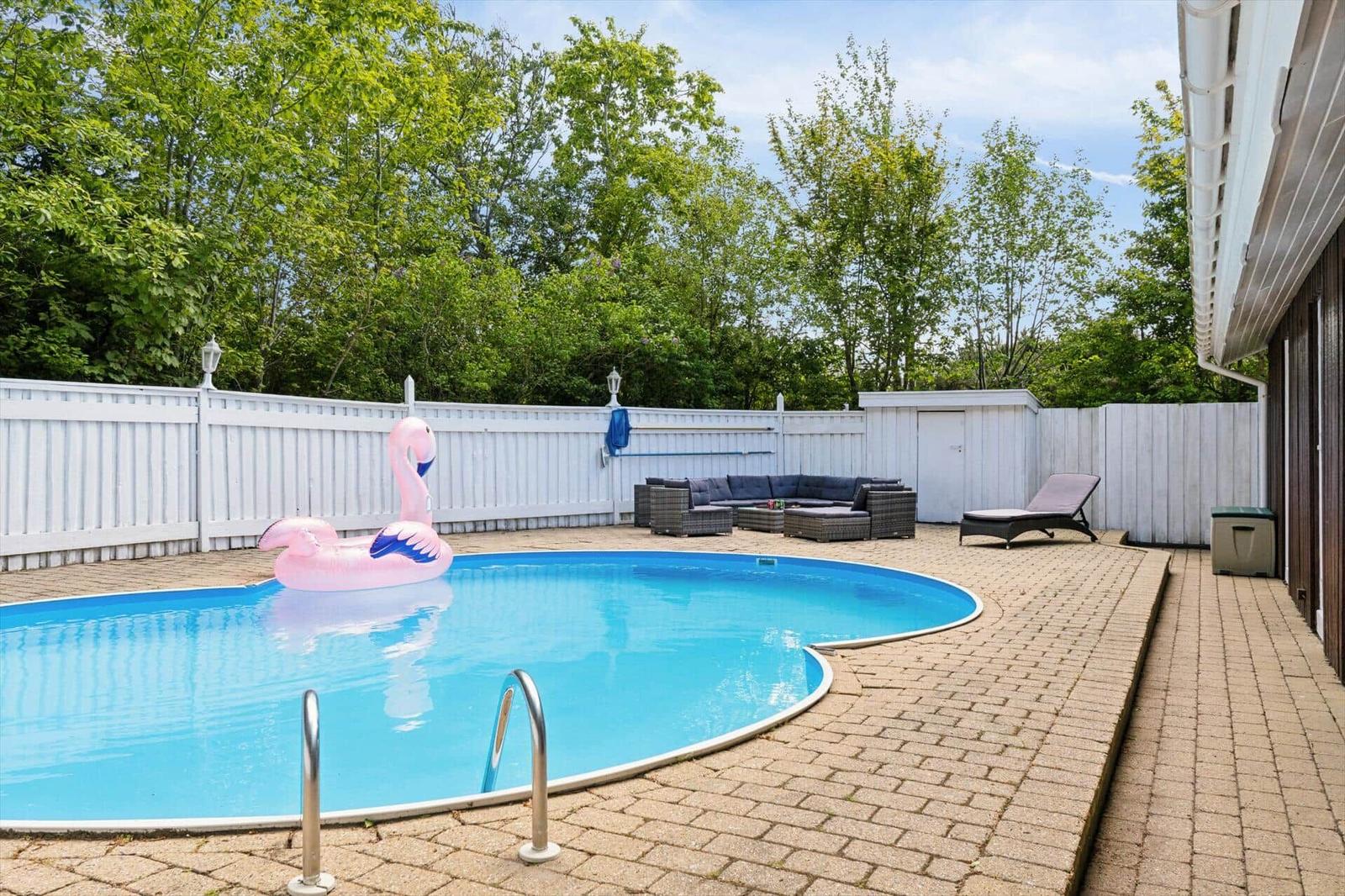Pool with pink flamingo, lounge area, and wooden house in background.