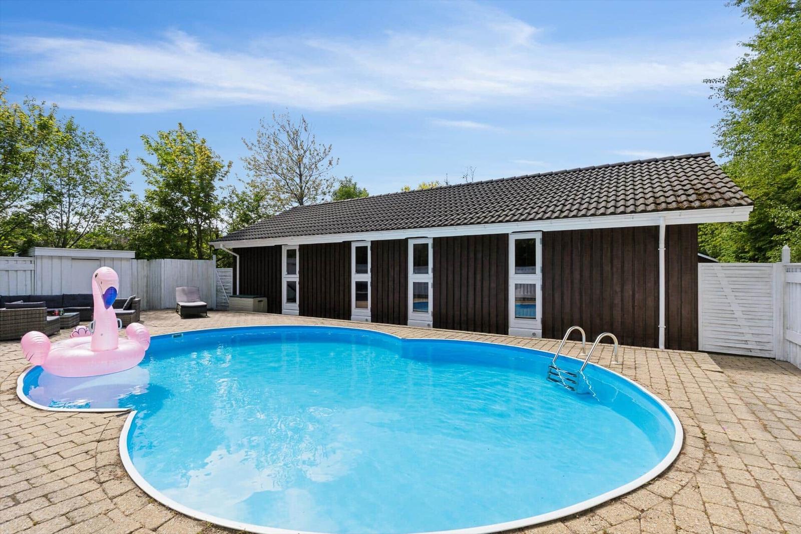 Pool with pink flamingo, terrace, and wooden house in background.