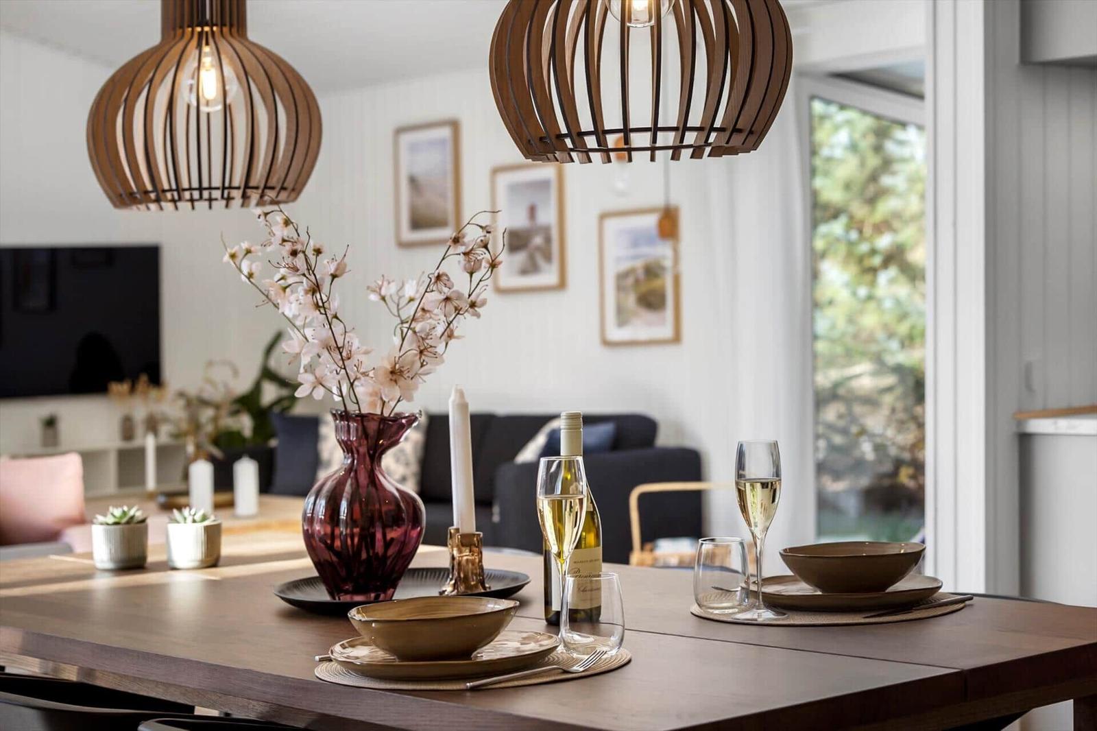 Dining table with wine, glasses, and vase under wooden lanterns.