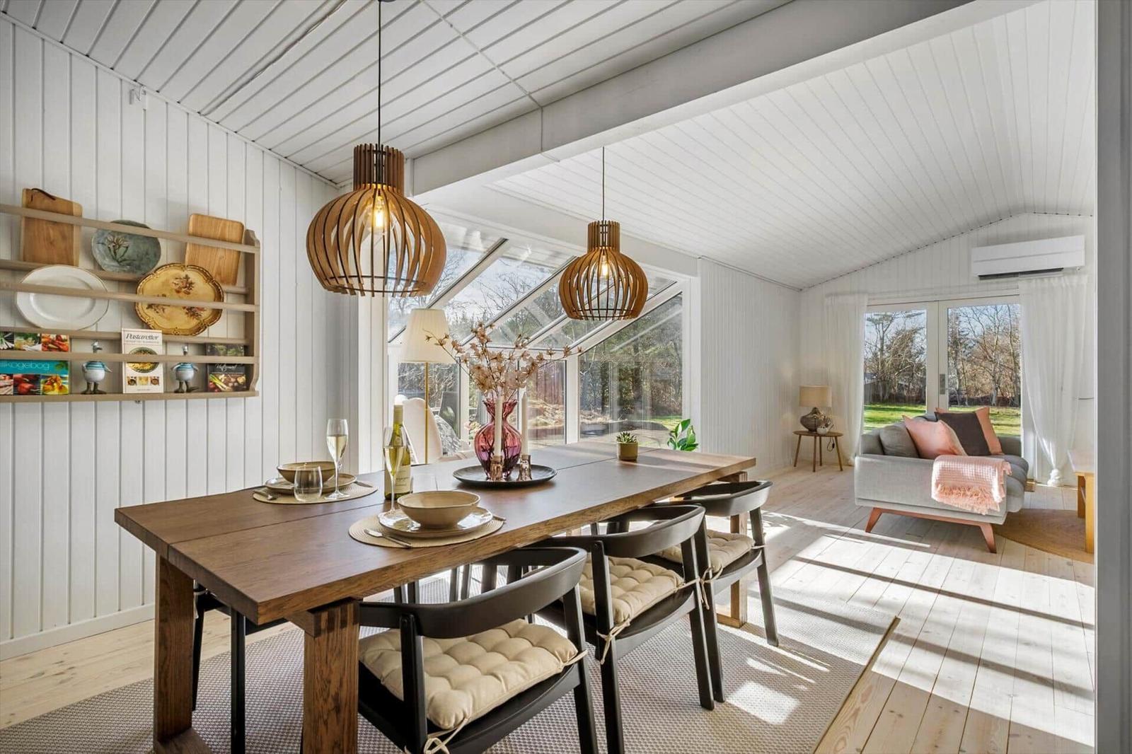 Dining area with table and chairs, view into living room with sofa and windows.