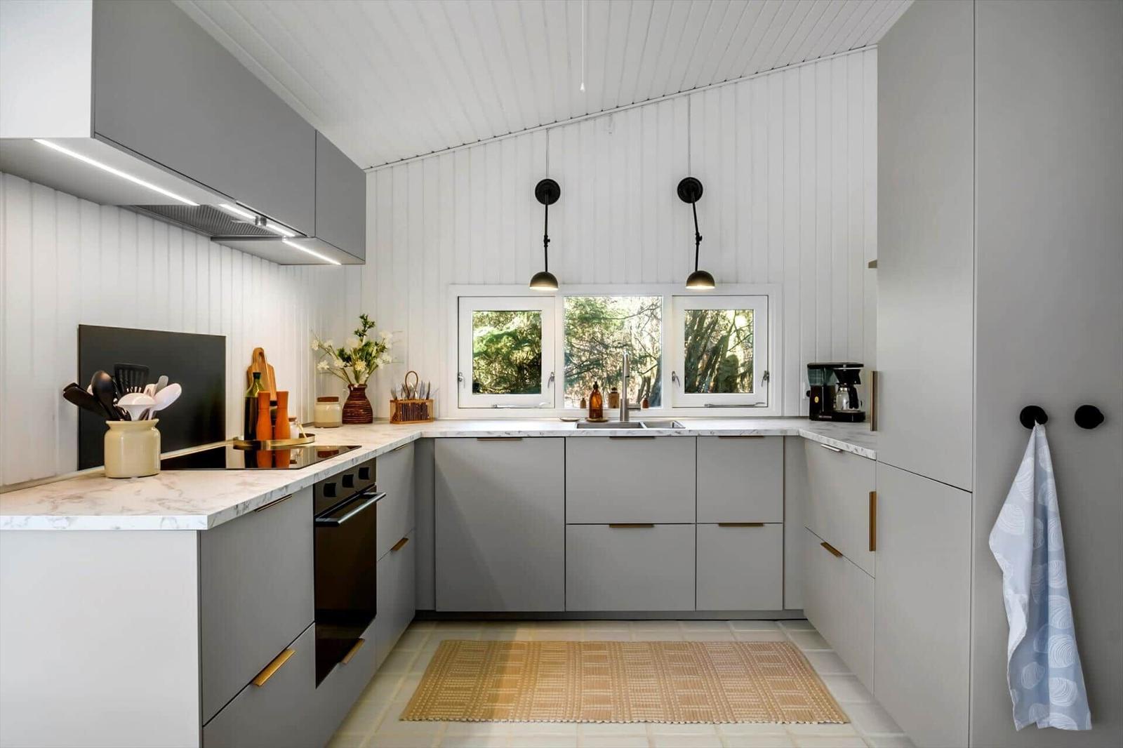 Modern kitchen with gray cabinets, marble countertop, and window with view of trees.
