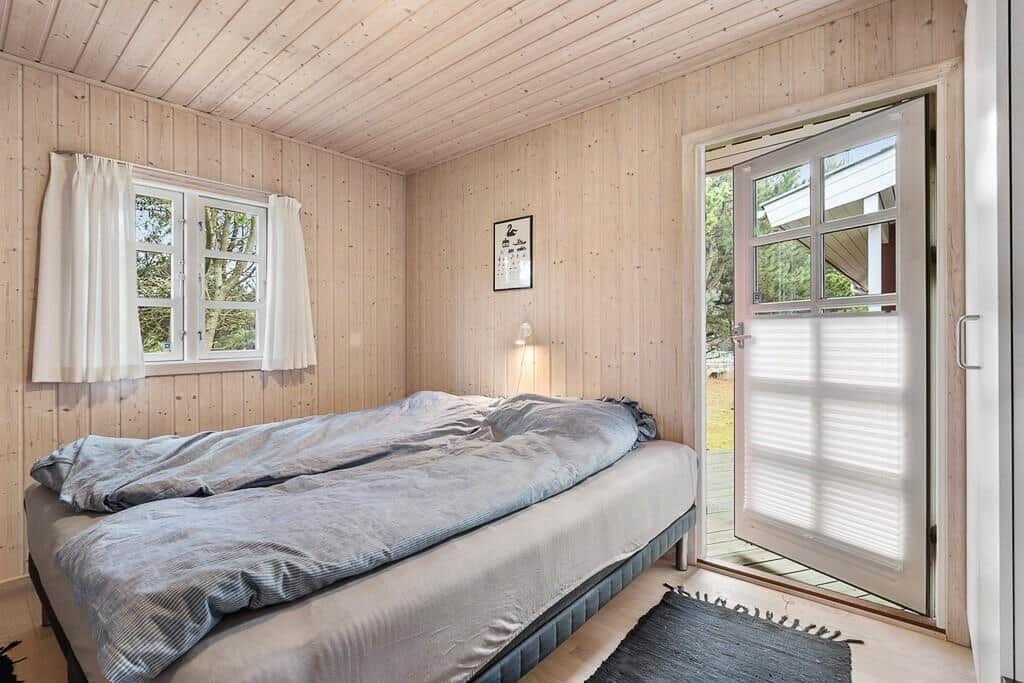 Schlafzimmer mit Holzwand, Bett und Tür zum Außenbereich.