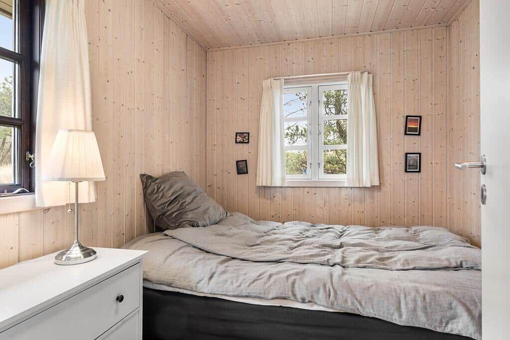 Schlafzimmer mit Holzwand, Bett, Nachttisch und Fenster.