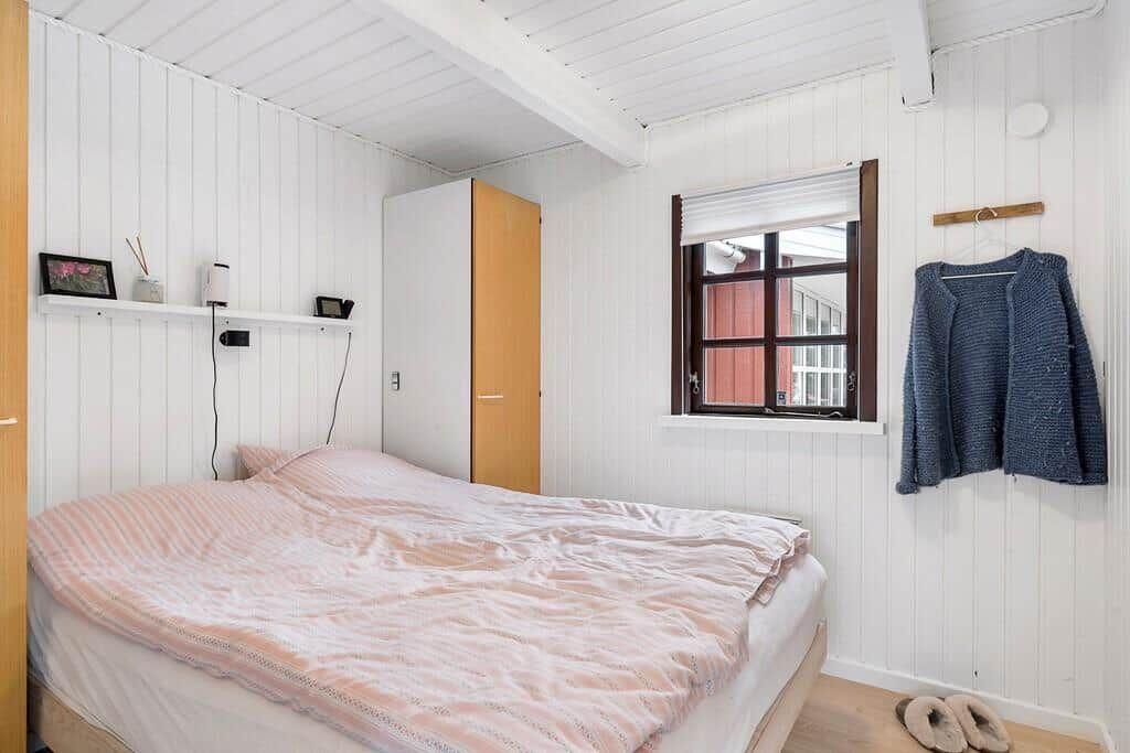 Schlafzimmer mit Bett, Kleiderhaken und Fenster. Wandverkleidung und Holzboden.