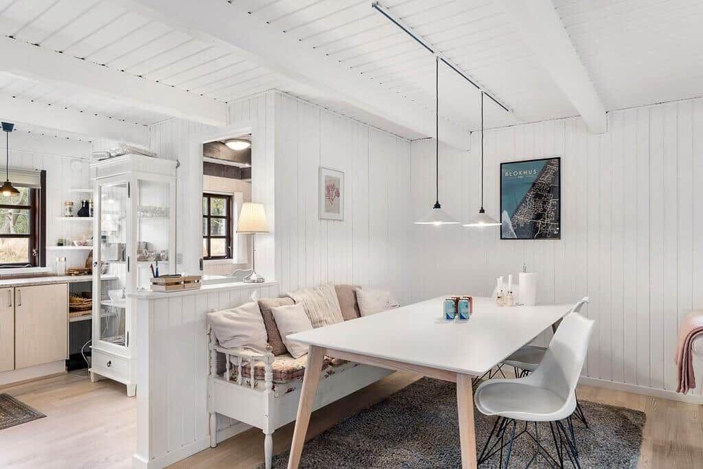 Essbereich mit Tisch, Stühlen und Sofa. Weiße Wände und Decke. Küchenbereich im Hintergrund.