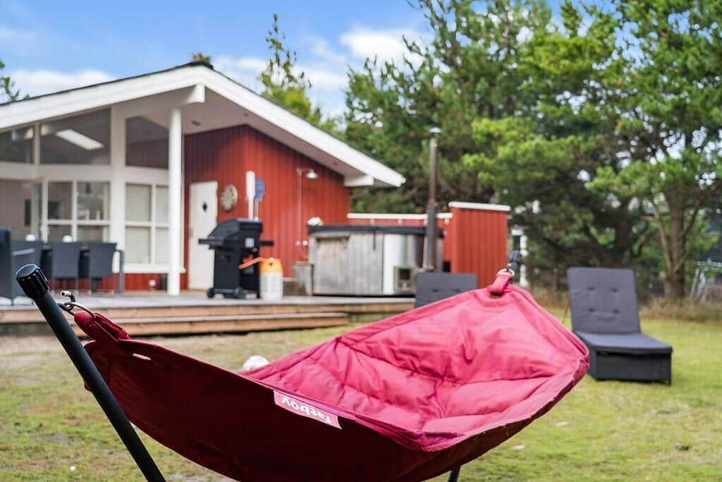 Roter Hängematte auf Gras vor rotem Haus mit Terrasse und Grill.
