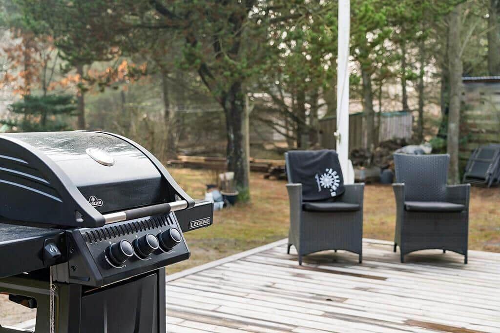 Gartenbereich mit Grill und zwei Sitzgelegenheiten auf Holzterrasse.